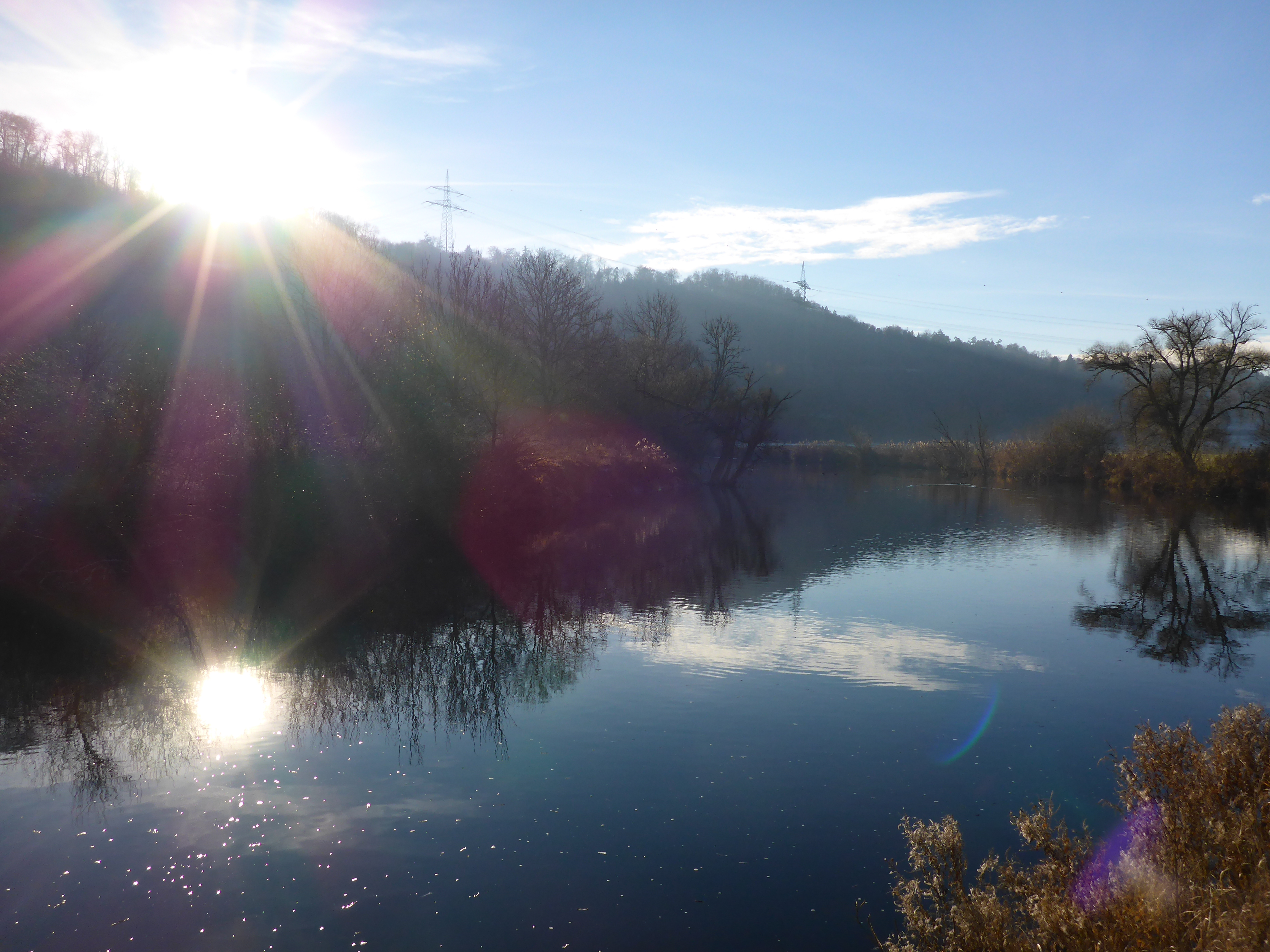 Das Foto zeigt den Neckar bei Rottenburg. Die Sonne spiegelt sich in Regenbogenfarben im Wasser.