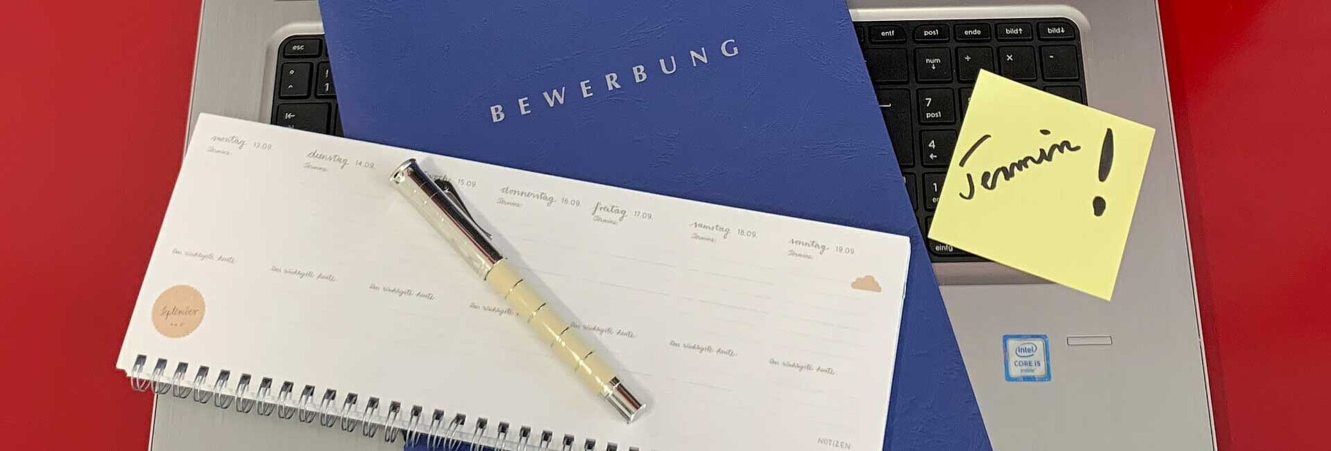 Bewerbungsmappe liegt auf einer Tastatur, daneben ein Terminkalender