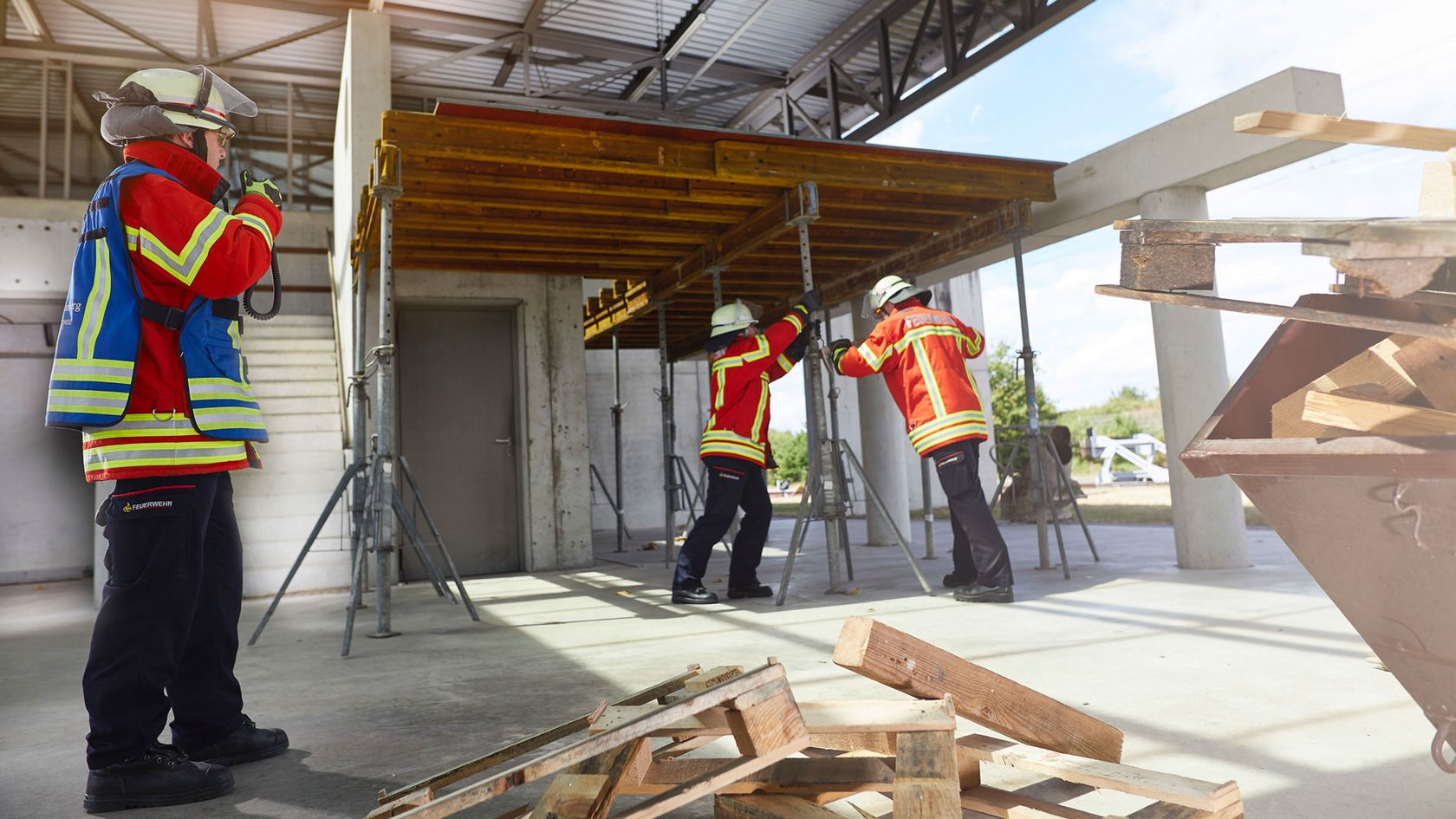 Übung auf der Anlage "Technische Hilfeleistung Bau". Zwei Einsatzkräfte stützen eine Baudecke ab, Einsatzleiter am Handsprechfunkgerät