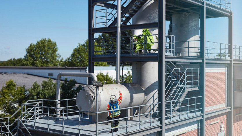 ABC-Übung auf der Chemie-Übungsanlage mit zwei Einsatzkräften in Schutzausrüstung auf einem Tankturm und dem Einsatzleiter auf der Ebene darunter.