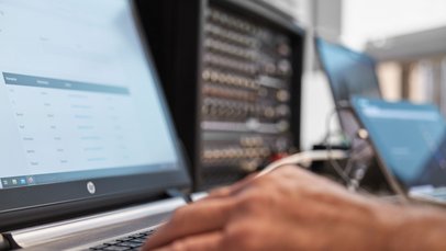 Hände am Laptop, im Hintergrund befinden sich weitere technische Geräte