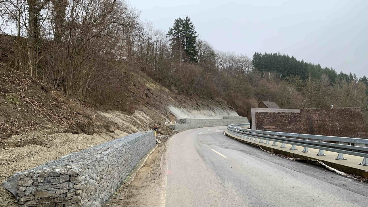 Das Foto zeigt die L 207. Links neben der Straße sieht man eine Gabionenwand unterhalb eines Hanges. Rechts der Straße sieht man Leitplanken..