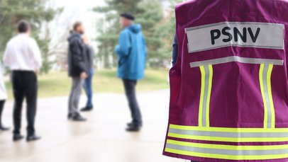 Person mit PSNV Weste, im Hintergrund eine kleine Gruppe ziviler Personen