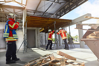Übung auf der Anlage "Technische Hilfeleistung Bau". Zwei Einsatzkräfte stützen eine Baudecke ab, Einsatzleiter am Handsprechfunkgerät