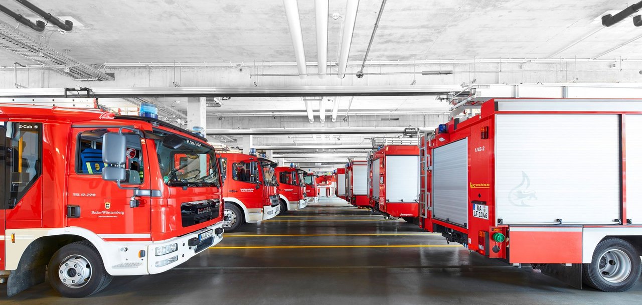 Blick in eine der Fahrzeughallen mit verschiedenen Lösch- und Einsatzfahrzeugen, geparkt in zwei Reihen hintereinander