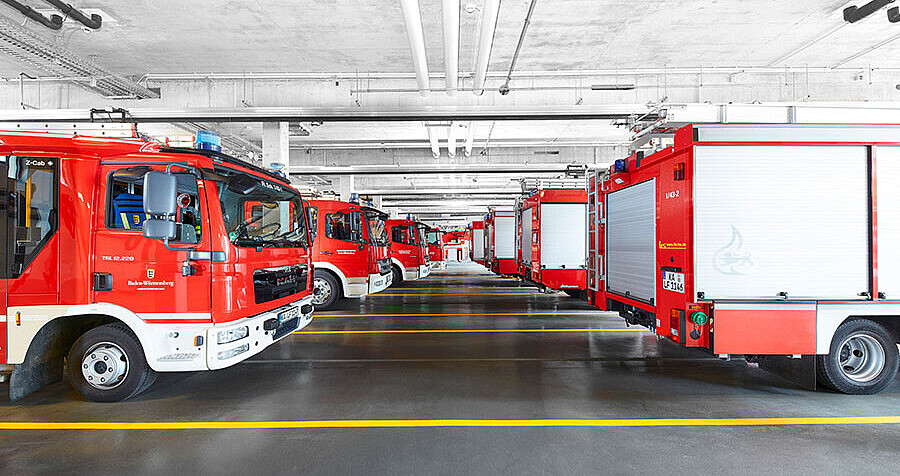Blick in eine der Fahrzeughallen mit verschiedenen Lösch- und Einsatzfahrzeugen, geparkt in zwei Reihen hintereinander