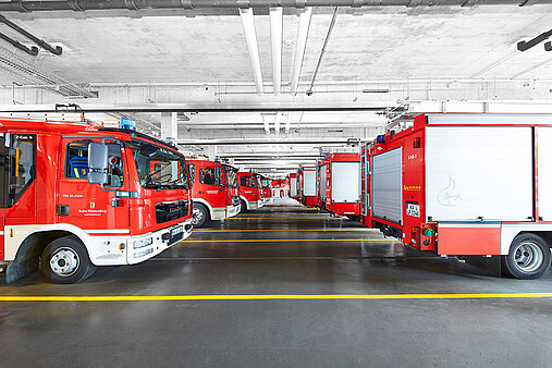 Blick in eine der Fahrzeughallen mit verschiedenen Lösch- und Einsatzfahrzeugen, geparkt in zwei Reihen hintereinander