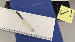 Bewerbungsmappe liegt auf einer Tastatur, daneben ein Terminkalender