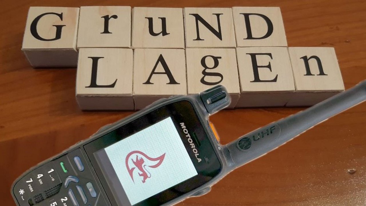 Buchstaben auf Holz die das Wort Grundlagen ergeben darunter ein Funkgerät